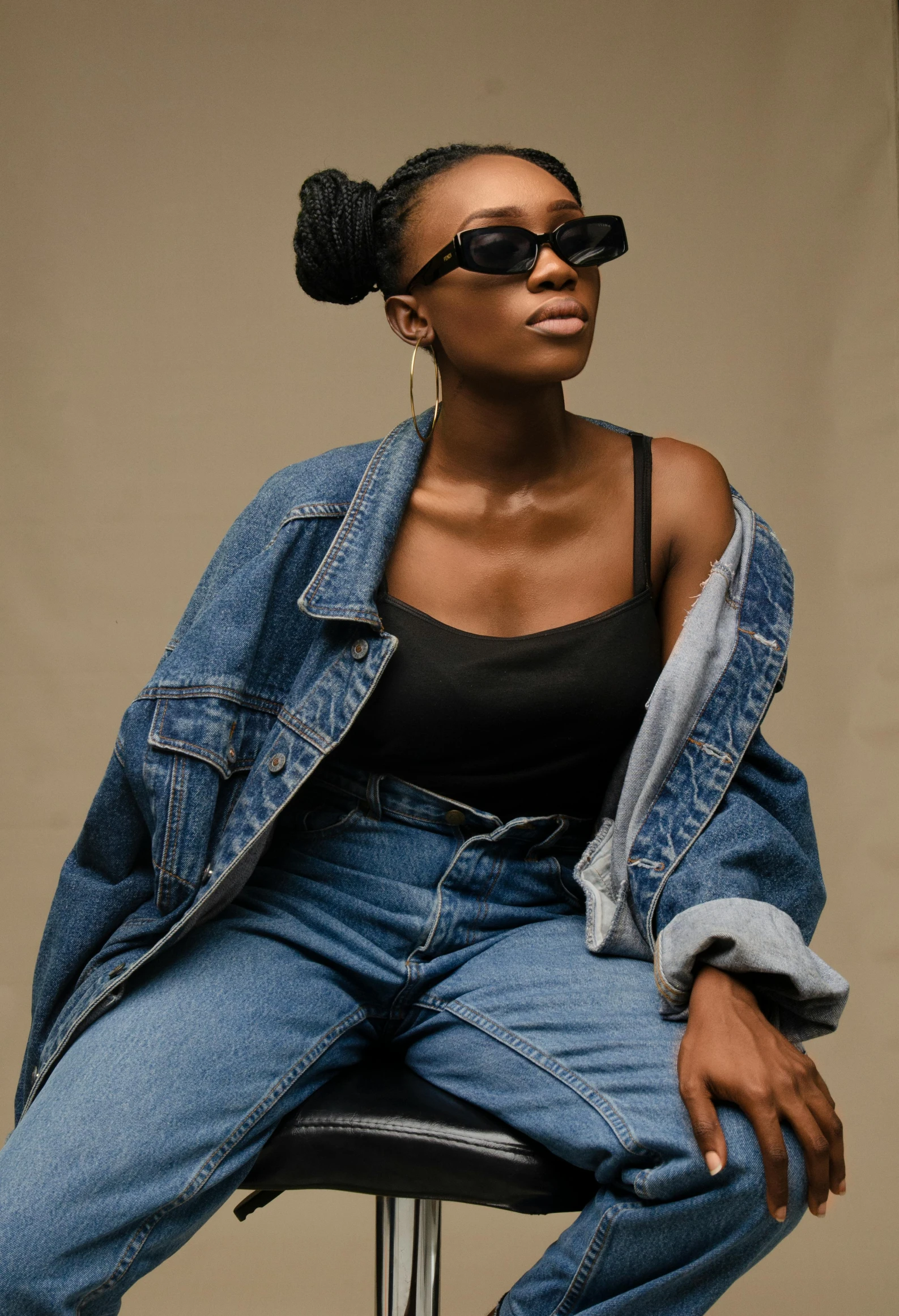 a woman sitting on top of a stool, by Lily Delissa Joseph, trending on pexels, wearing a jeans jackets, wearing shades, ( ( dark skin ) ), old fashion