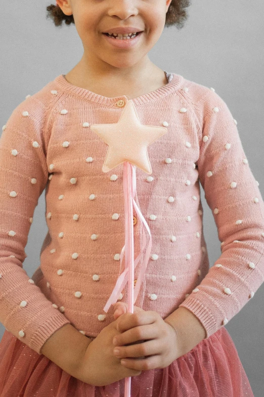 a little girl in a pink dress holding a star wand, inspired by Annabel Kidston, tactile buttons and lights, wearing a designer top, medium close up shot, full product shot