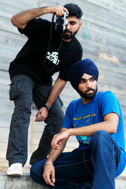 a man taking a picture of another man on a skateboard, an album cover, inspired by Manjit Bawa, hurufiyya, blue-black, wearing a tee shirt and combats, official store photo, in a fighting pose