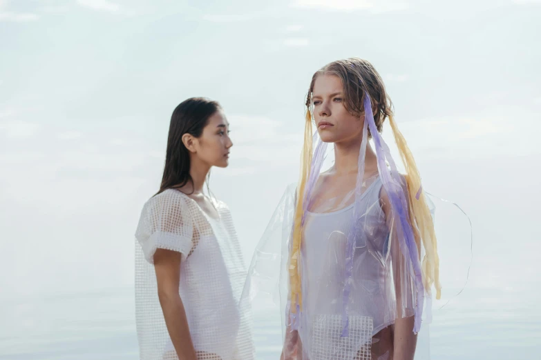 two women standing next to each other on a beach, by Emma Andijewska, gutai group, wearing translucent veils, aurora aksnes and zendaya, ignant, violet polsangi