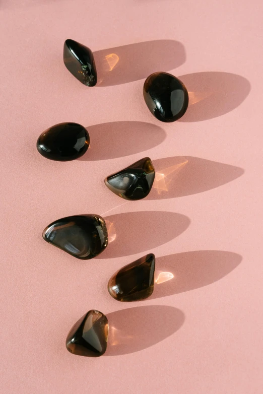 a group of black stones sitting on top of a pink surface, by Lisa Milroy, trending on pexels, plasticien, translucent gills, amber jewelry, hair jewellery, smooth oval shape face