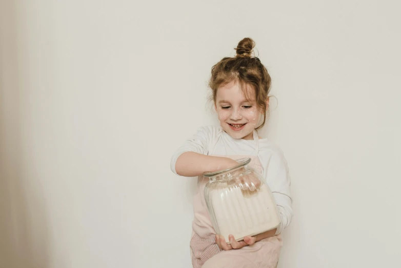 a little girl sitting on a stool holding a jar, pexels contest winner, cream white background, flour dust, having a good time, gif