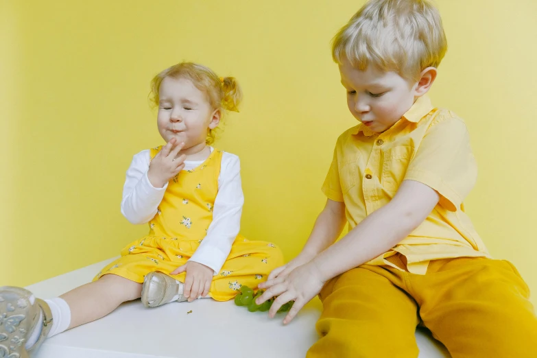 a couple of kids sitting on top of a table, pexels, yellow overall, crispy quality, lena oxton, indoor picture