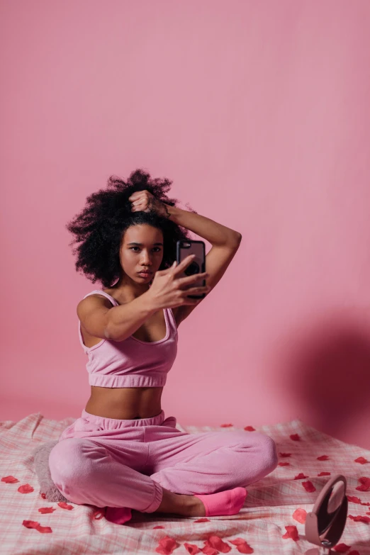 a woman sitting on a bed holding a cell phone, by Cosmo Alexander, trending on pexels, happening, tight gigantic pink curls, wearing a tracksuit, woman with black hair, concept photoset