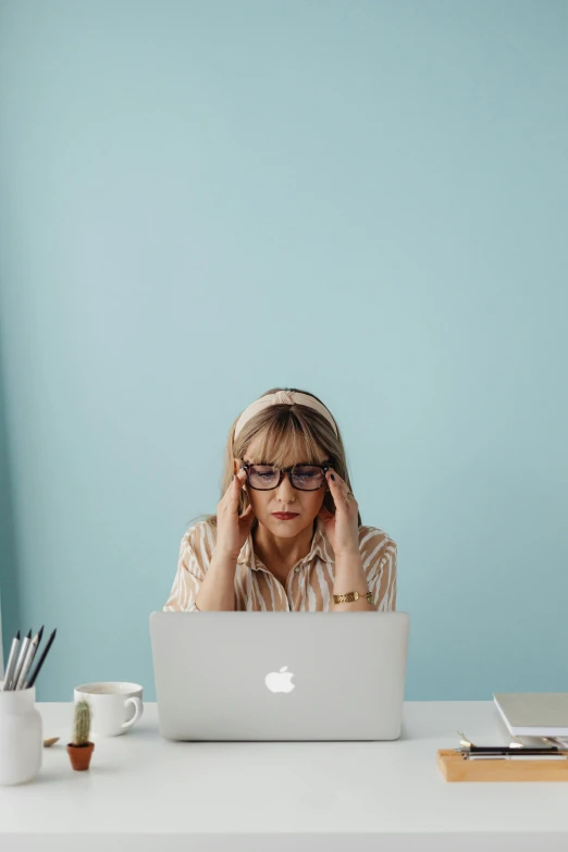 a woman sitting in front of a laptop computer, by Paul Bird, pexels, looking exhausted, wearing small round glasses, a blond, stacked image