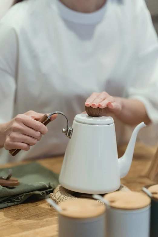 a woman pouring tea into a white tea pot, inspired by Kanō Shōsenin, unsplash, process art, with a wooden stuff, designer product, brown, ivory