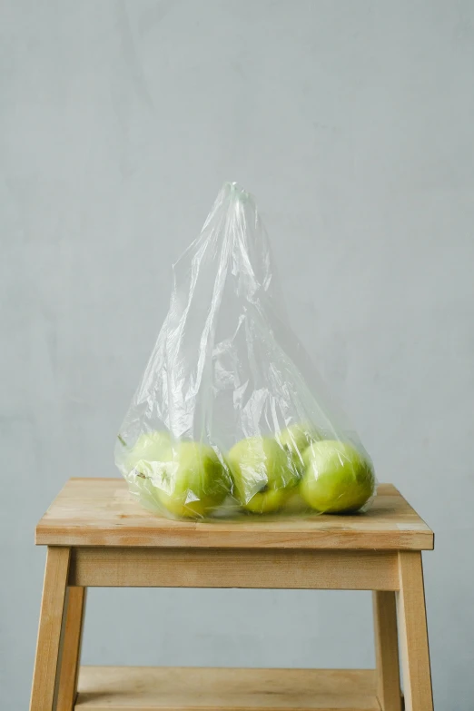 a bag of apples sitting on top of a wooden stool, in plastic, lime, no text, small