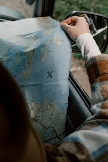 a person sitting in a car looking at a map, by Jesper Knudsen, teaser, worn, coastal, college