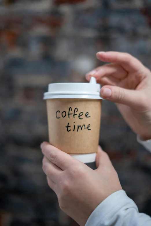 a person holding a cup of coffee with the word coffee time written on it, by Robbie Trevino, label, thumbnail, colour photograph, day time