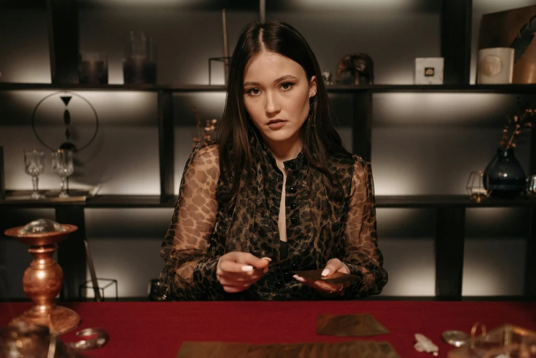 a woman sitting at a table holding a cell phone, a magician's chamber, occult inspired, keng lye, high quality photo