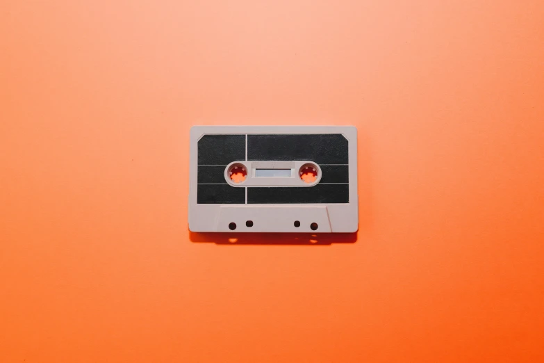 a close up of a cassette on an orange background, trending on pexels, on a gray background, paper cut out, 🎨🖌️, magnetic