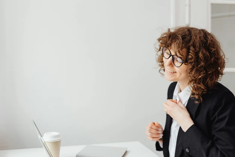 a woman sitting at a table in front of a laptop computer, by Nicolette Macnamara, trending on pexels, wearing a suit and glasses, curly haired, girl standing, on a white table