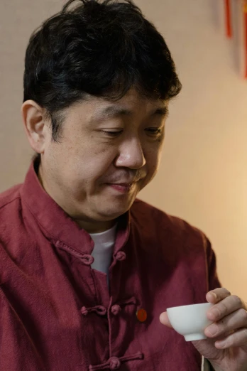 a man in a red shirt holding a white cup, inspired by Chen Daofu, shin hanga, drinking tea, up close shot shinji aramaki, hotei is on the table, kaigetsudo ando