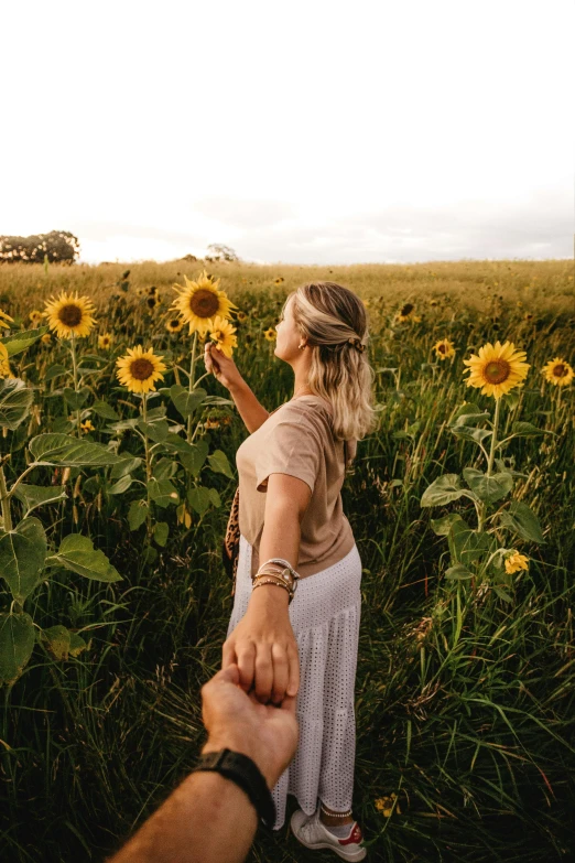 a woman holding a man's hand in a field of sunflowers, pexels contest winner, blonde, australian wildflowers, looking into the horizon, instagram picture