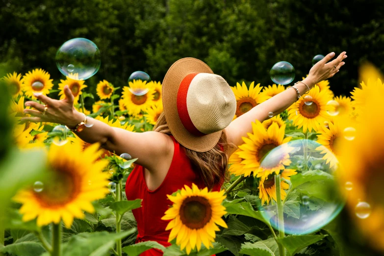 a woman in a sunflower field blowing bubbles, by Julia Pishtar, pexels contest winner, arms open, 🦩🪐🐞👩🏻🦳, vibrant scene, holiday season