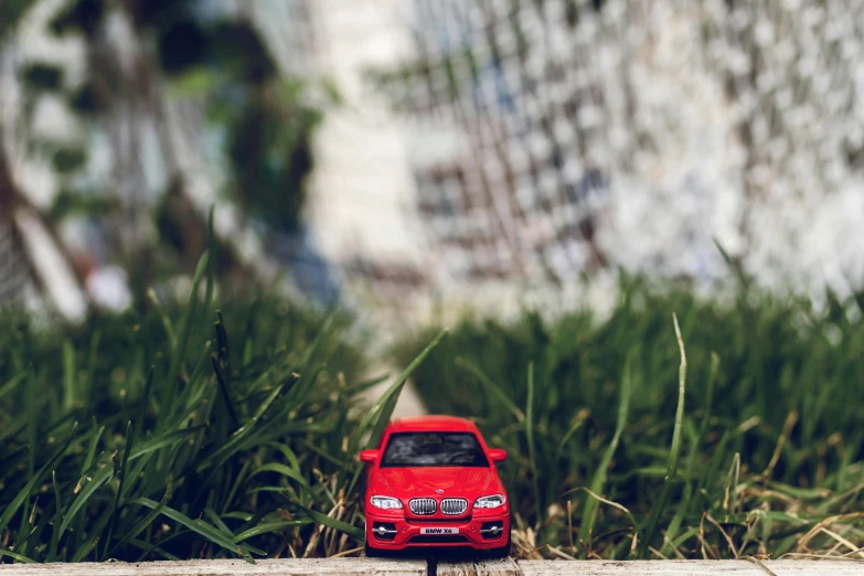 a toy car that is sitting in the grass, a tilt shift photo, pexels contest winner, photorealism, red car, “2019 bmw m5 wagon, sitting on a miniature city, rule of thirds