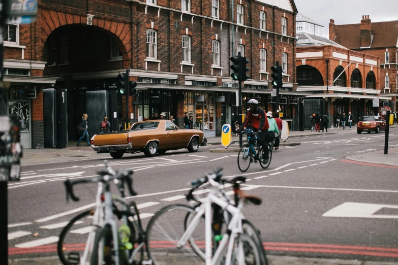 a couple of people riding bikes down a street, by Nina Hamnett, pexels contest winner, london streets in background, cars parked underneath, square, carrington