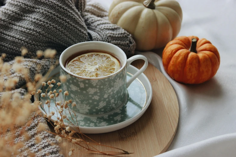 a cup of coffee sitting on top of a saucer, a still life, trending on pexels, rococo, pumpkins, green tea, cozy under a blanket, lemon