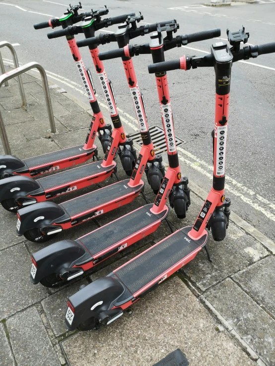 a row of electric scooters parked on a sidewalk, taken from the high street, it has a red and black paint, thumbnail, gracked