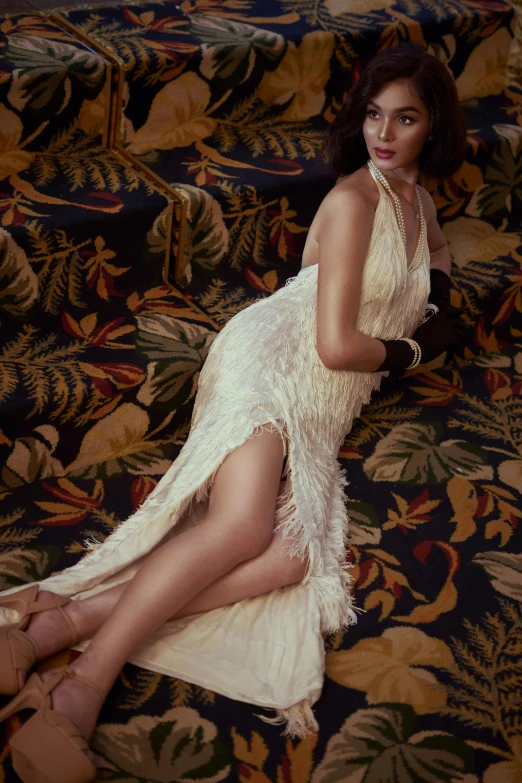 a woman in a white dress sitting on a couch, an album cover, inspired by George Hurrell, trending on pexels, arabesque, ostrich feathers, elegant tropical prints, kiko mizuhara, fullbody view