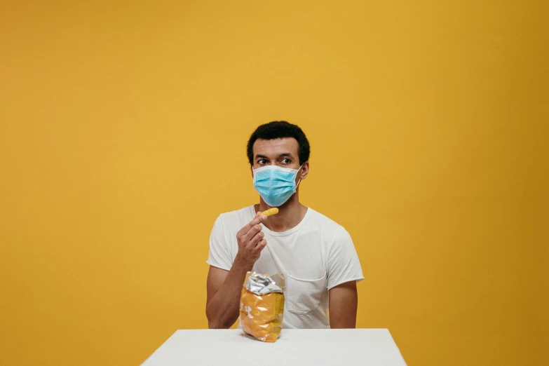 a man sitting at a table wearing a face mask, pexels contest winner, yellow theme, having a snack, avatar image, studio shoot