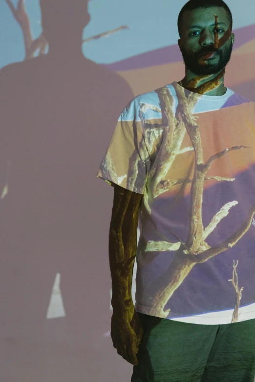 a man standing in front of a projection of a tree, an album cover, inspired by Ren Hang, pexels contest winner, violet coloured t-shirt, sunfaded, close up half body shot, ( ( dark skin ) )