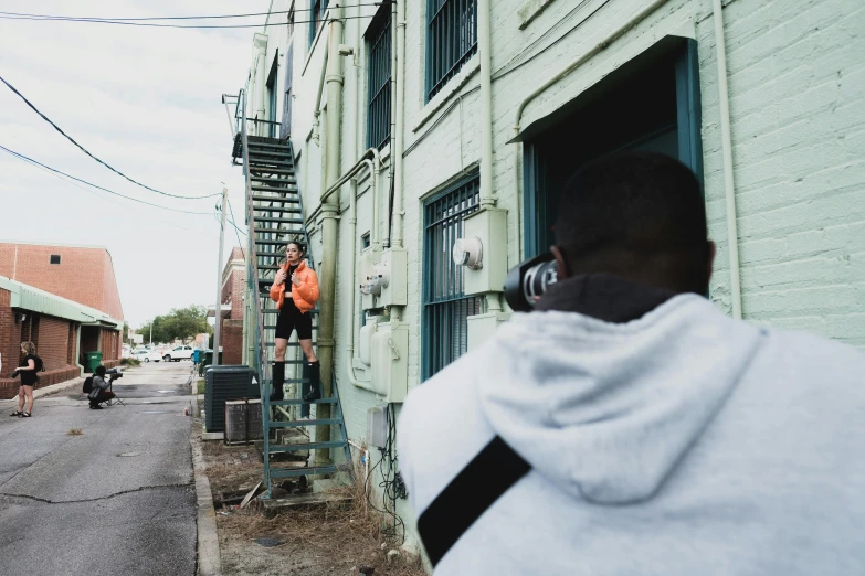 a man standing on a ladder in front of a building, a photo, happening, behind the scenes photography, teddy fresh, arik roper, in an alley