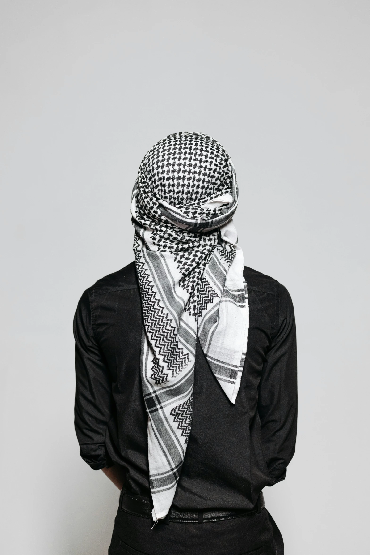 a man in a black shirt and a white scarf, inspired by Farid Mansour, unsplash, patterned clothing, on grey background, ffffound, covered head