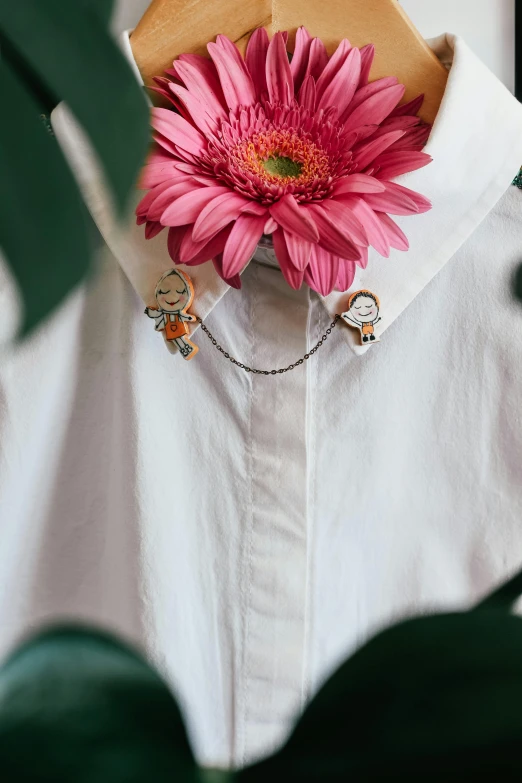 a pink flower sitting on top of a white shirt, a cartoon, inspired by Elsa Bleda, wearing several pendants, calvin and hobbes, detail shot, wearing steel collar