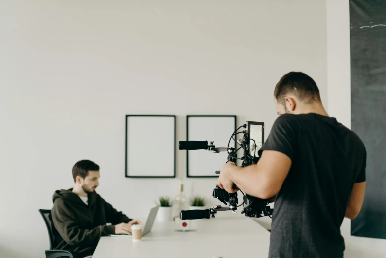 a man sitting at a table with a camera in front of him, trending on pexels, video art, medium shot of two characters, people at work, movie setup, professional image