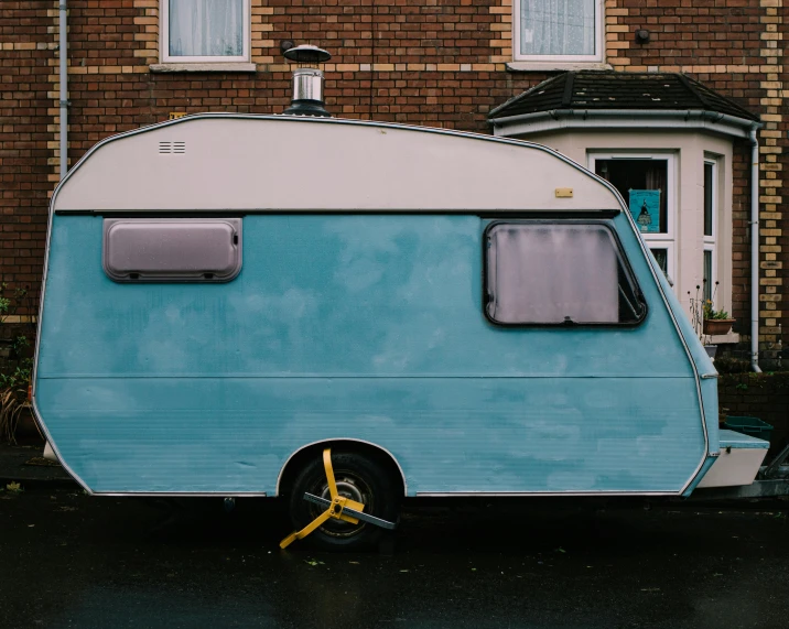 a blue and white trailer parked in front of a brick building, by Carey Morris, trending on unsplash, caravan, square, beaten, brown and cyan color scheme