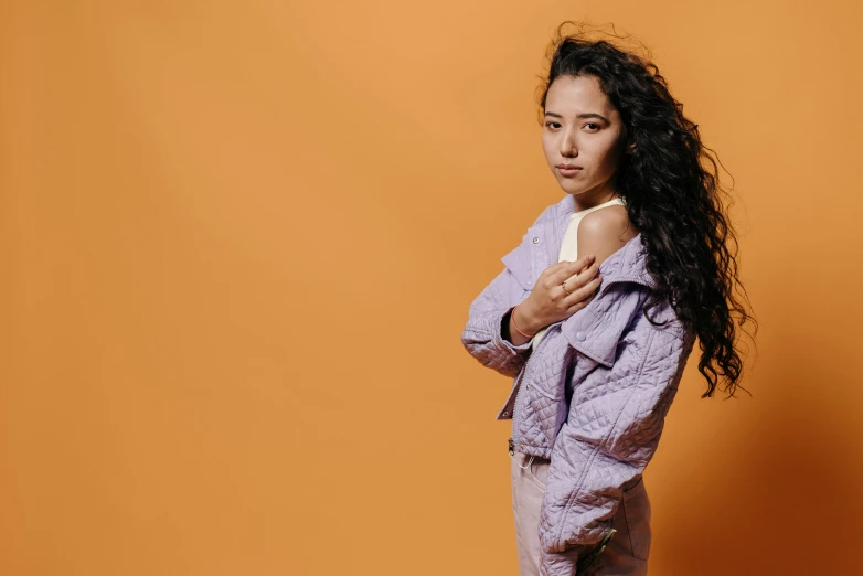 a woman standing in front of an orange background, inspired by Kim Tschang Yeul, trending on pexels, rococo, purple leather jacket, mixed race, on grey background, teenage girl