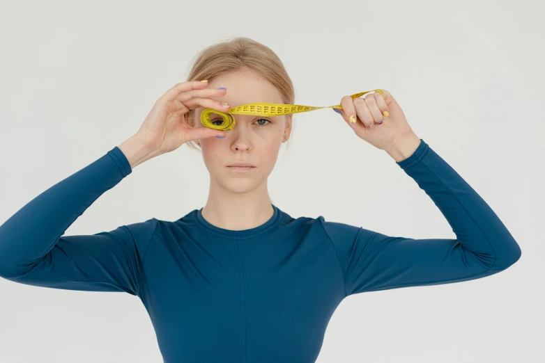 a woman holding a measuring tape over her eyes, inspired by Vanessa Beecroft, unsplash, sport clothing, square jaw-line, neuroscience, scaled arm