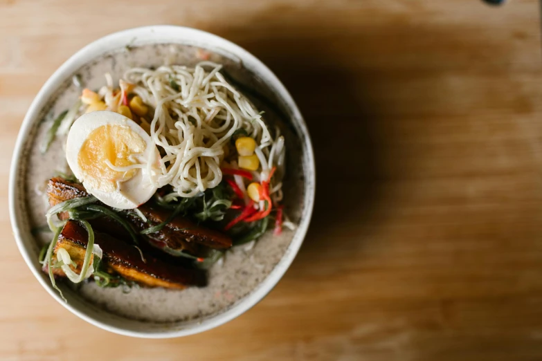 a bowl of food sitting on top of a wooden table, unsplash, mingei, light grey, creamy, south east asian with long, a colorful