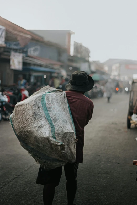 a man walking down a street carrying a large bag, pexels contest winner, indonesia, mining, cold, marketplace