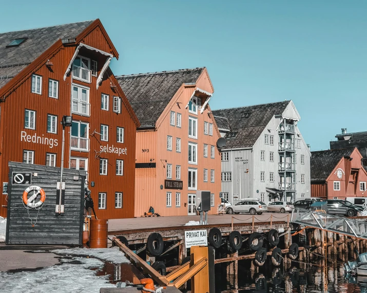 a row of buildings next to a body of water, by Christen Dalsgaard, pexels contest winner, gray and orange colours, scandinavian / norse influenced, shipyard, 🦩🪐🐞👩🏻🦳