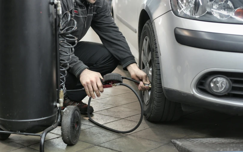 a man working on a tire in front of a car, shutterstock, les automatistes, low pressure system, high quality picture, hoses:10, thumbnail