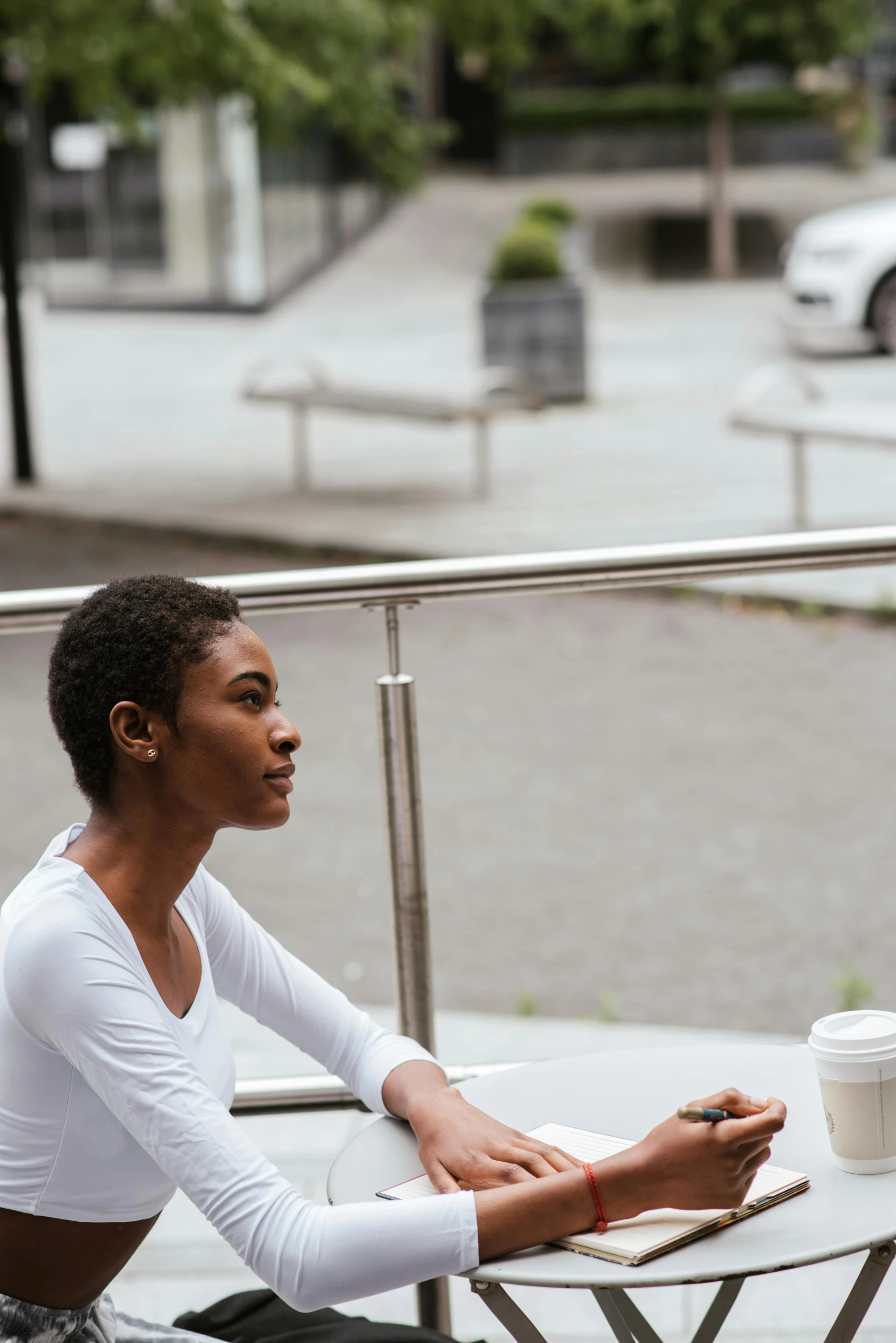 a woman sitting at a table with a cup of coffee, by Nina Hamnett, trending on unsplash, happening, beautiful city black woman only, looking to the right, outside, multiple stories