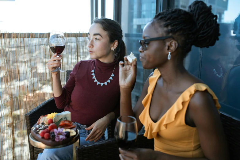 two women sitting at a table with a plate of food and a glass of wine, by Carey Morris, pexels contest winner, on a balcony, beautiful city black woman only, charli bowater and artgeem, eating a cheese platter