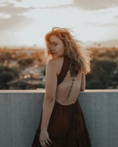 a woman standing on top of a cement wall, inspired by Elsa Bleda, trending on pexels, renaissance, ginger wavy hair, open back dress, queer woman, wearing a low cut tanktop