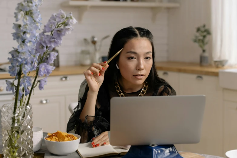 a woman sitting at a table with a laptop and a bowl of food, trending on pexels, hyperrealism, asian face, holding pencil, low quality photo, fashionable