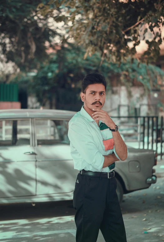 a man standing in front of a parked car, a colorized photo, inspired by Saurabh Jethani, pexels contest winner, realism, thin moustache, confident stance, greenish tinge, headshot profile picture