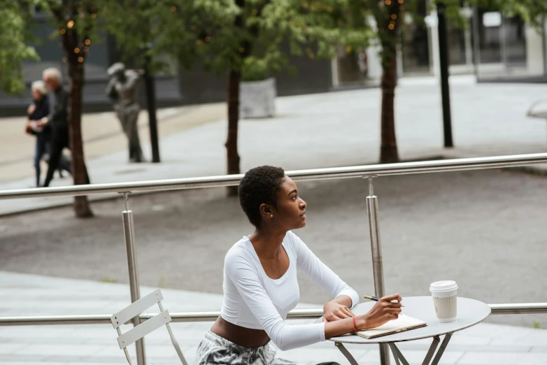 a woman sitting at a table with a cup of coffee, beautiful city black woman only, people outside eating meals, lena oxton, relaxed posture