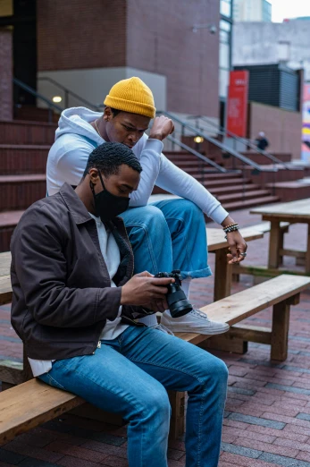a couple of men sitting on top of a wooden bench, a picture, by Washington Allston, unsplash, black arts movement, holding a camera, people are wearing masks, college students, [ theatrical ]