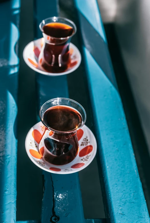 two cups of tea sit on a blue bench, hurufiyya, maroon and blue accents, detailed shot legs-up, syrup, deep colour