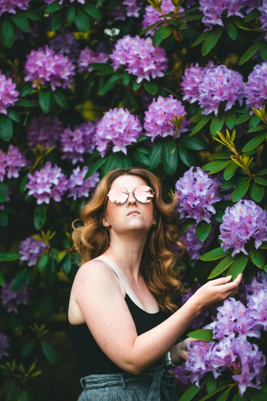 a woman standing in front of a bush of purple flowers, by Carey Morris, pexels contest winner, wearing mirrored sunglasses, hr ginger, wavy hair spread out, 2019 trending photo