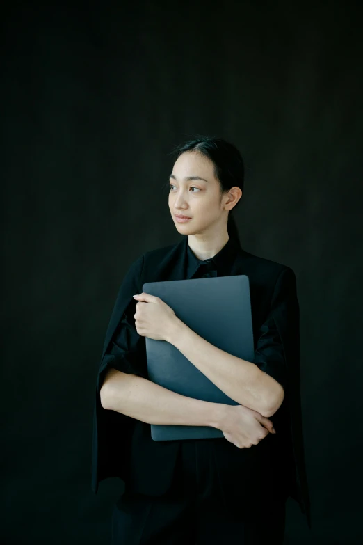 a woman holding a laptop computer in her hands, an album cover, inspired by Fei Danxu, unsplash, neo-figurative, wearing a black noble suit, matte black paper, ai researcher, a portrait of issey miyake