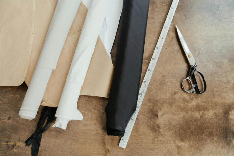 a pair of scissors sitting on top of a piece of paper, a still life, inspired by Sarah Lucas, trending on pexels, arts and crafts movement, leather trench coat, holding a thick staff, folds of fabric, white and black color palette