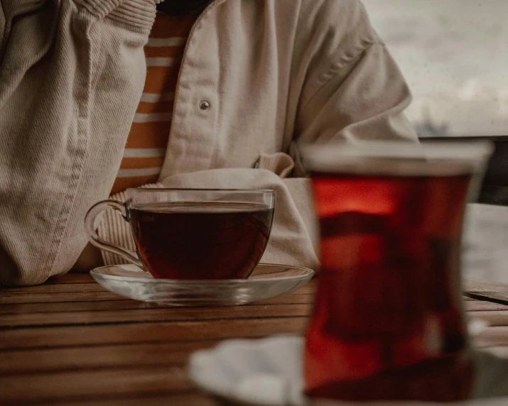 a man sitting at a table with a cup of tea, trending on pexels, maroon and white, mysterious coffee shop girl, manuka, from waist up