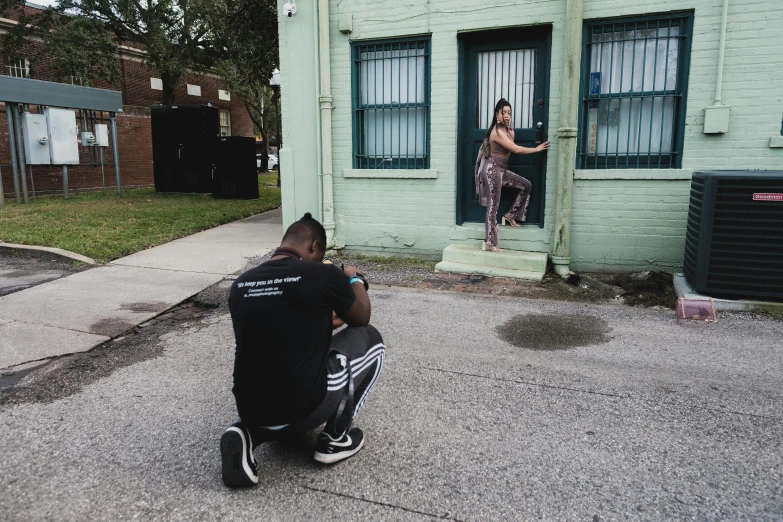 a man kneeling down in front of a building, a photo, by Andrew Stevovich, realism, behind the scenes photography, modeling for dulce and gabanna, teddy fresh, standing in a township street